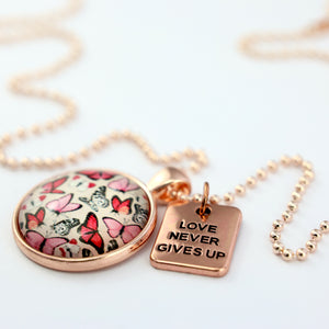 Pink floral print circle pendant rose gold necklace with ball chain with 'love never gives up' word charm. Fundraising product for the National Breast Cancer Foundation. 