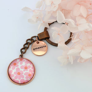 Pink floral print vintage red copper circle keychain with 'strength' charm. A product that fundraises for the National Breast Cancer Foundation. 