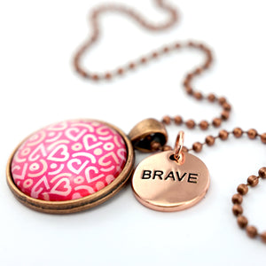 Pink heart print vintage red copper circle pendant necklace with 'brave' charm. A fundraising product for the national breast cancer foundation. 