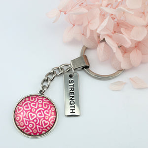 Pink heart print silver keychain pendant with strength charm. A fundraising product for the national breast cancer foundation. 